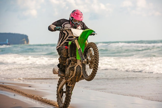 Motociclista haciendo un caballito en la playa